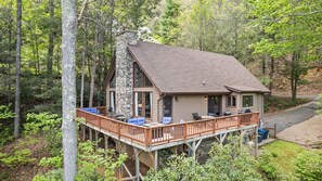 A cabin with a stone exterior, a deck with outdoor seating, and a view of the surrounding forest. - Lanfyne Ayr / Views / Gameroom (Waynesville)