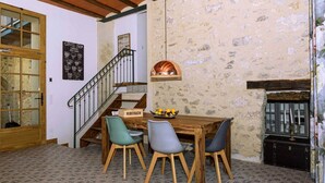 Un comedor con mesa y sillas de madera, una escalera y una pared rústica de piedra.