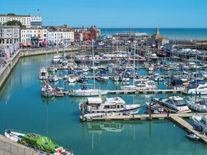 Un port de plaisance où sont amarrés de nombreux bateaux, une promenade en bord de mer et des bâtiments en arrière-plan.