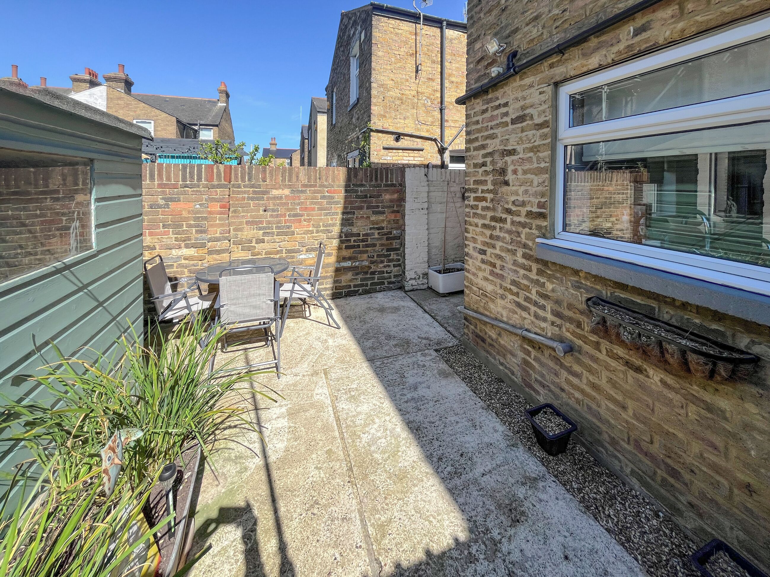 A small patio area with a table and chairs, a brick wall, and a window.