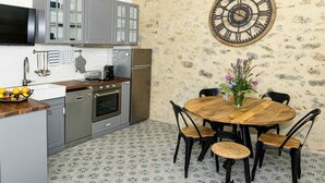 Eine Küche mit grauen Schränken, einer Holz Arbeitsplatte, einem Edelstahlbackofen, einer an der Wand befestigten Uhr und einem Esstisch mit Stühlen.