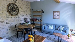 Ein gemütliches Wohnzimmer mit einer Steinwand, einem Holzespeisetisch mit Stühlen, einem blauen Sofa mit gemusterten Kissen und einer Wanduhr.