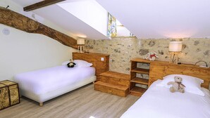 Una habitación acogedora con dos camas, cabeceros de madera, una pared de piedra y un tragaluz.
