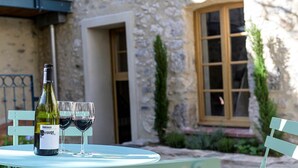 A stone building with a window and a door, a bottle of wine, and two glasses on a table. - La Grange Droite Cottage 3 Stars (BELESTA)