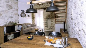 A rustic interior with exposed stone walls, a wooden dining table set with breakfast, and a loft-style sleeping area. - La Grange Droite Cottage 3 Stars (BELESTA)