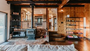 Un intérieur chaleureux avec un poêle à bois, une cheminée en briques et un escalier menant à un étage supérieur.