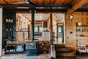 A cozy interior with a wood-burning stove, a brick fireplace, and a staircase leading to an upper level.