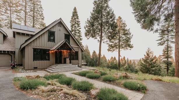 Ein modernes, zweistöckiges Haus mit einer markanten Veranda, eingebettet in eine natürliche Landschaft mit hohen Bäumen.
