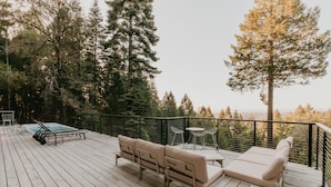 Eine Holzterrasse mit Gartenmöbeln, einem Whirlpool und Blick auf einen Wald.