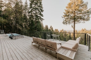 Une terrasse en bois avec des meubles d’extérieur, un jacuzzi et une vue sur une forêt.