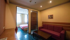 A hotel room with a wooden floor, a red sofa, a small table, and a bed with a wooden headboard. - Yunjiang Business Hotel (Shanghai Nanle Road Branch) (Shanghai)