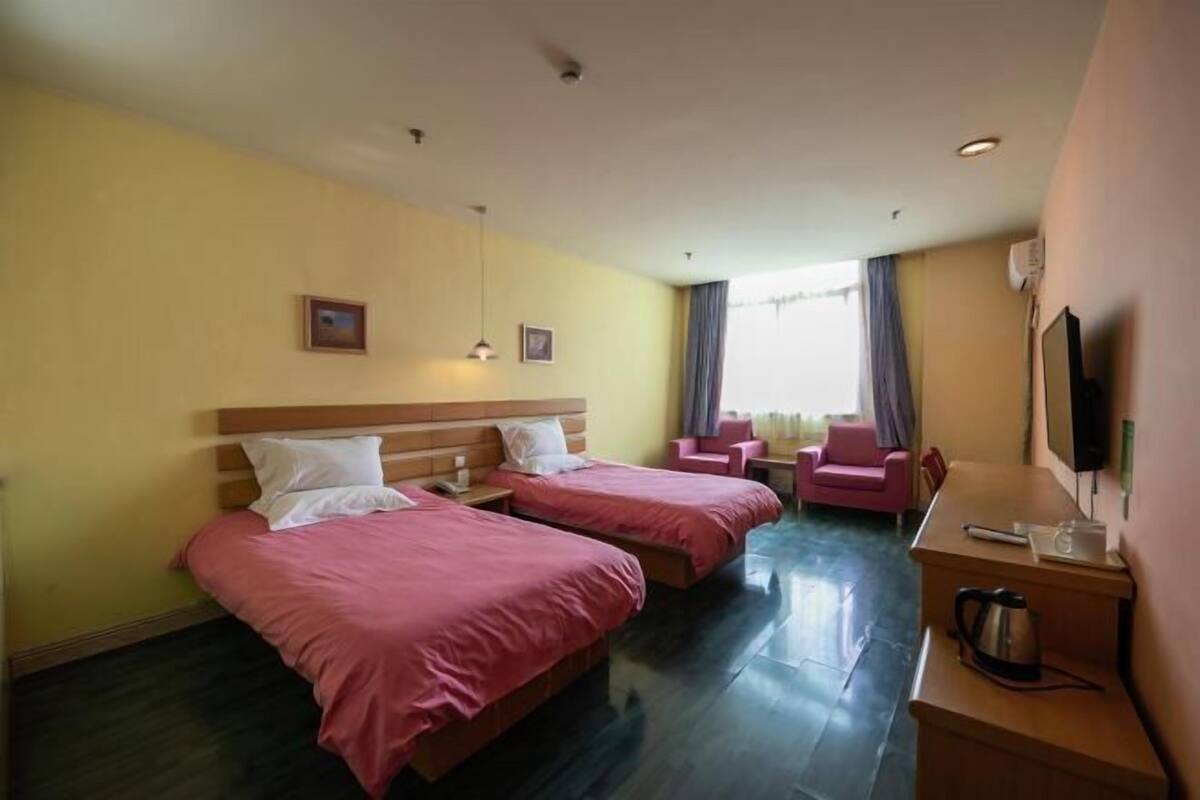 A hotel room with two beds, a desk, a chair, and a TV.