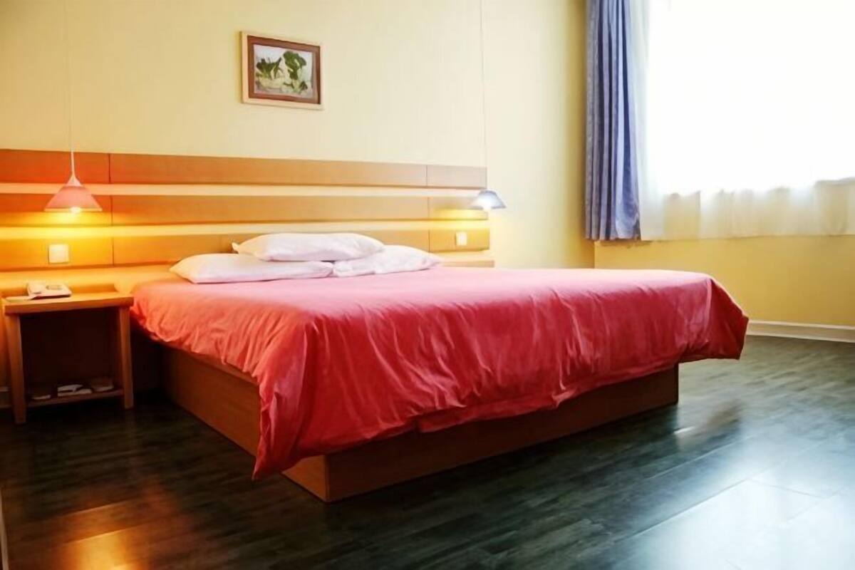 A hotel room with a bed, bedside lamps, a nightstand, a wall-mounted picture, and a window with curtains.