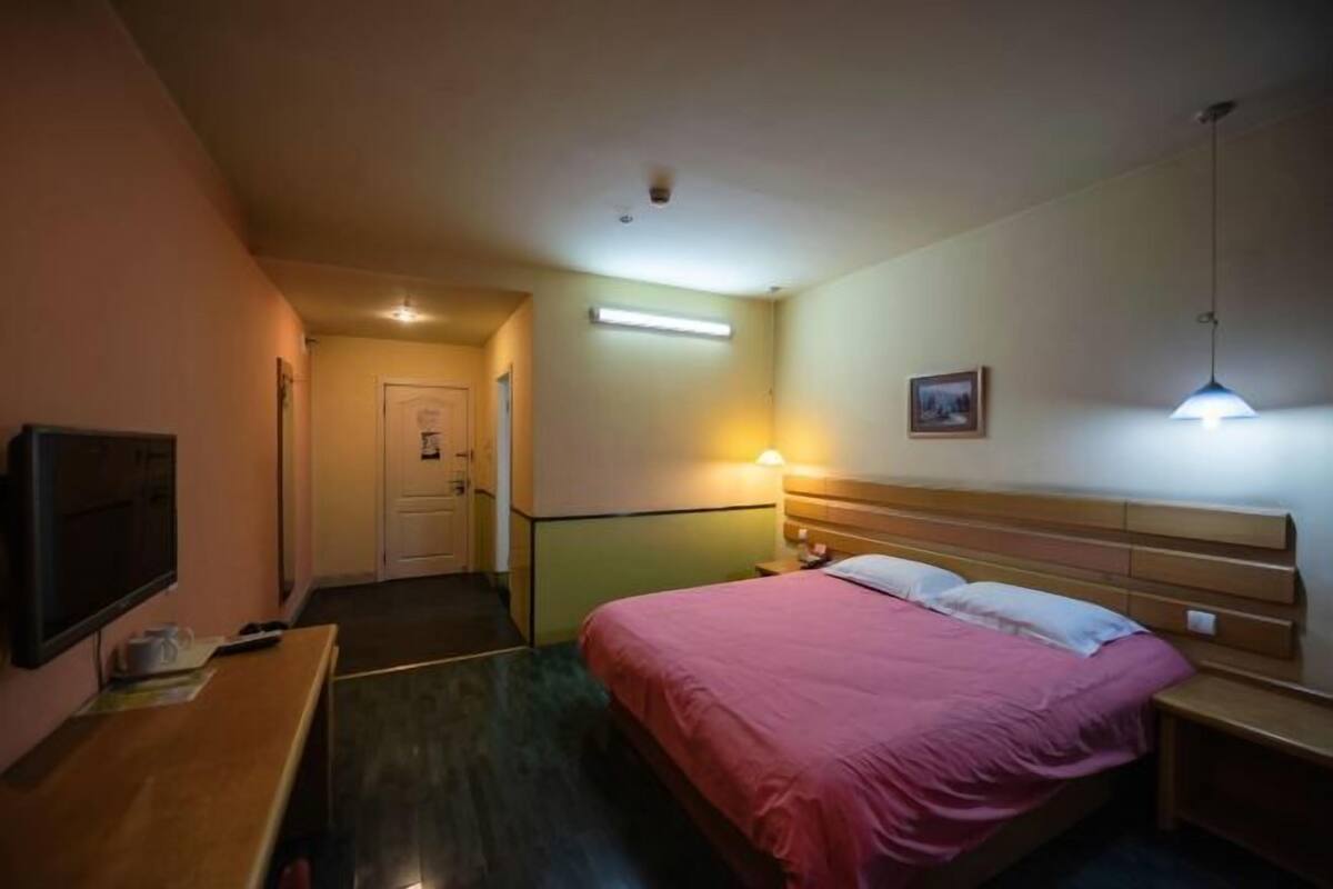 A hotel room with a bed, bedside table, lamp, and a television on a stand.