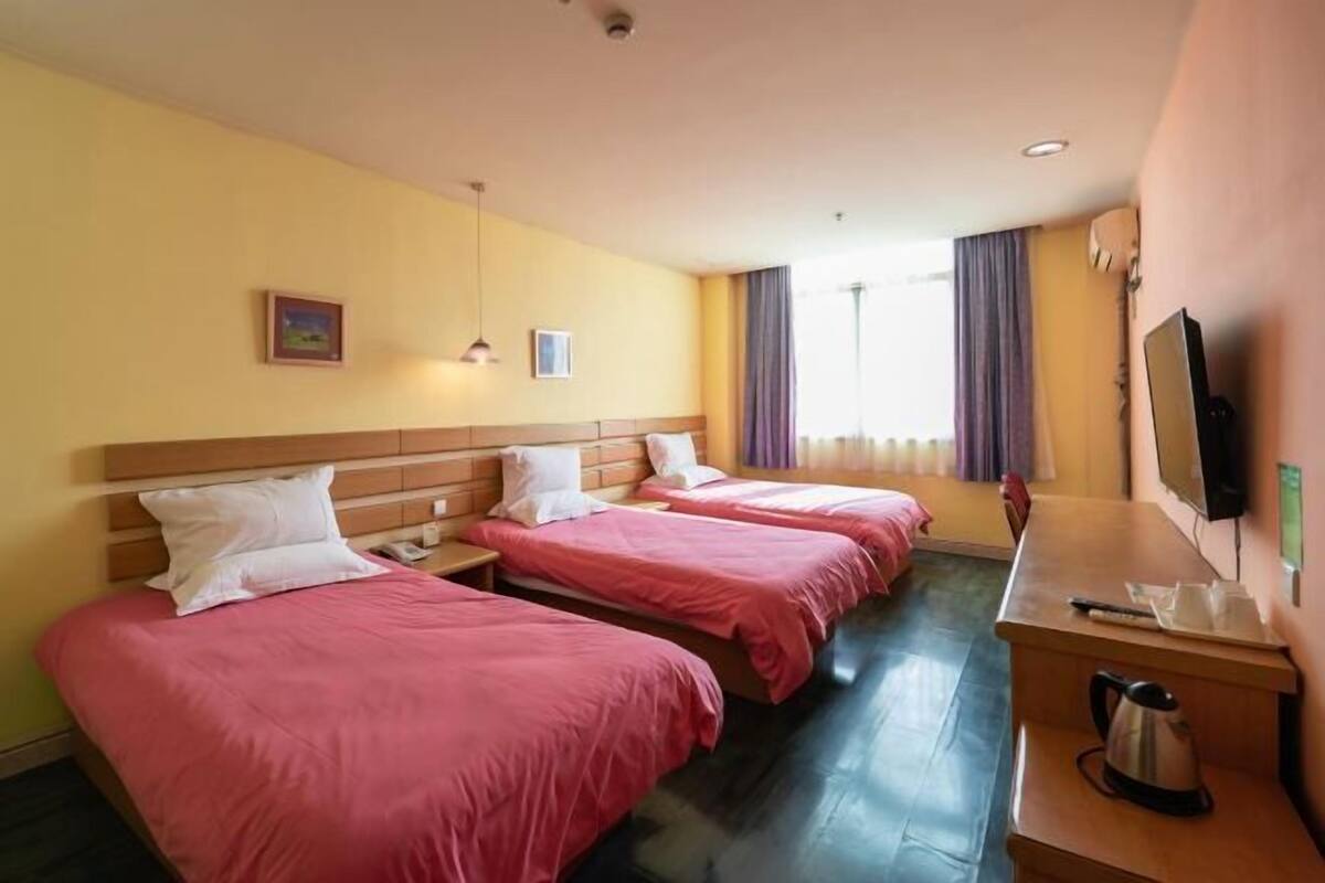 A hotel room with three beds, a wooden desk, a television, and a window with curtains.