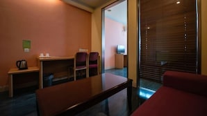 A hotel room with a wooden table, two chairs, a red sofa, a small desk with a kettle, and a television. - Yunjiang Business Hotel (Shanghai Nanle Road Branch) (Shanghai)
