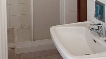 Une salle de bain avec un lavabo blanc, un miroir, une cabine de douche et un porte-serviettes.