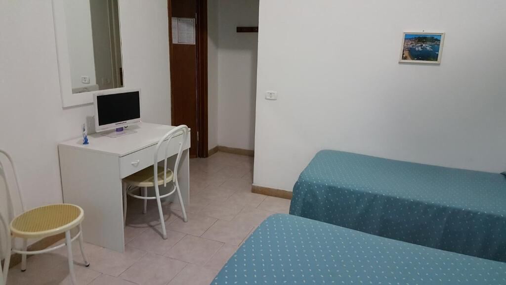Ein Schlafzimmer mit einem Bett, einem Schreibtisch mit Computer, einem Stuhl und einem kleinen Tisch.