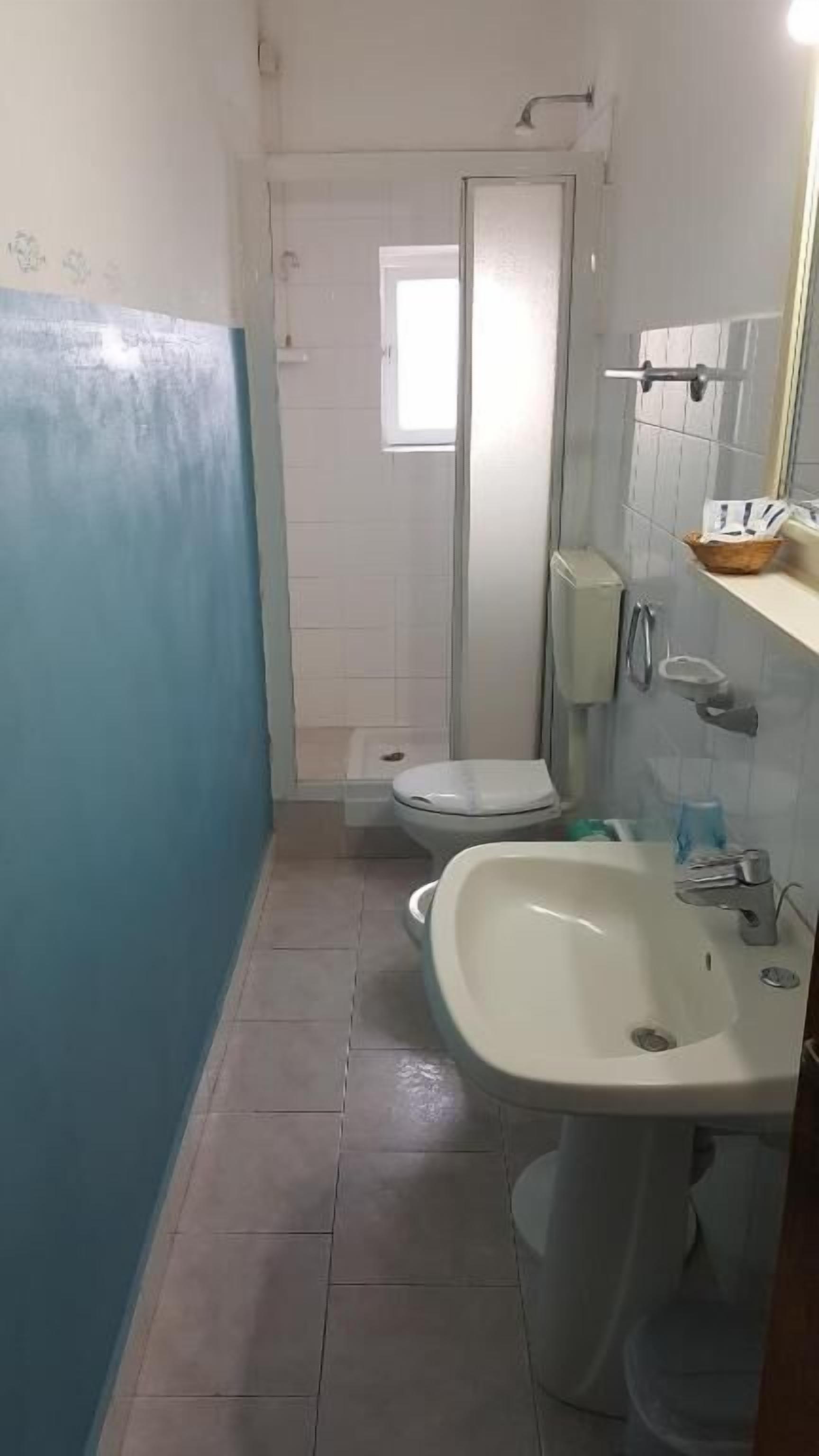 A narrow bathroom with a toilet, sink, and a window.