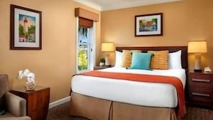 A hotel room with a large bed, two bedside lamps, a nightstand with a vase, and a chair. - Charming studio in Key West -Close to Duval.  Beautiful Pool area. (Key West)