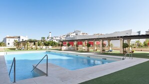 Une piscine dotée d’une zone abritée, entourée d’une pelouse bien entretenue et bordée d’une rangée de bâtiments en arrière-plan.