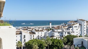 Une ville côtière aux bâtiments blancs, dotée d’un port de plaisance et surplombée d’un ciel bleu azur.