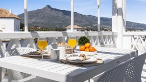 Un espace extérieur, de couleur blanche, aménagé pour les repas, avec une table dressée pour le petit-déjeuner, offrant une vue sur un paysage montagneux.