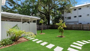 Un patio trasero bien cuidado con cerca blanca, un pérgola y un árbol pequeño.