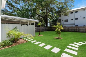 Un jardin bien entretenu, avec une clôture blanche, une pergola et un petit arbre.