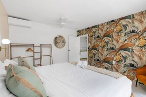 Une chambre à coucher avec un lit, des oreillers, une armoire, un miroir rond et un ventilateur de plafond.