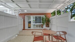 Un patio cubierto al aire libre con una mesa y sillas, una planta en maceta y vistas hacia una habitación contigua.
