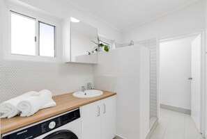Un baño moderno con un lavamanos blanco, encimera de madera y lavadora integrada.