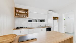 Una cocina moderna con armarios blancos, encimera de madera y un portátil sobre la mesa.