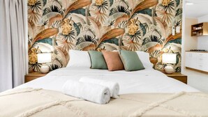 Una cama bien hecha con sábanas blancas, una toalla enrollada y varios almohadones de diferentes colores.