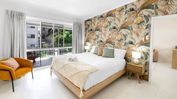 Una habitación de hotel moderna con una cama grande, un balcón y un papel tapiz con motivos tropicales.