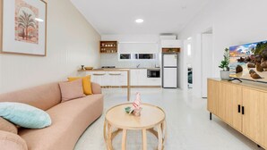 Una sala moderna con un sofá, una mesa redonda de madera y una cocina al fondo.