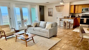 Ein Wohnzimmer mit grauem Sofa, Couchtisch aus Holz und Blick auf den Ozean durch große Schiebetüren.