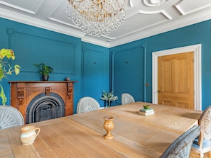 A dining room with a wooden table, chairs, a chandelier, and a blue wall.