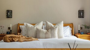 Ein ordentlich bezogenes Bett mit Holz-Kopfteil, ein Nachttisch mit Kerze und ein dekorativer Korb mit Kerzen.