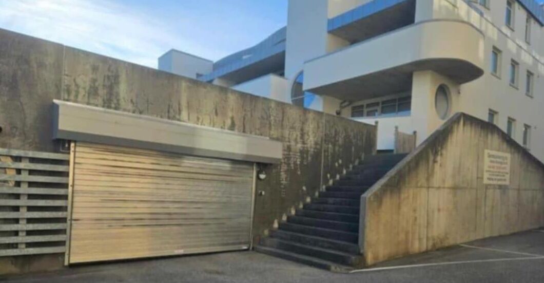 A building with a closed garage door, a set of stairs leading to an upper level, and a concrete wall with a sign.