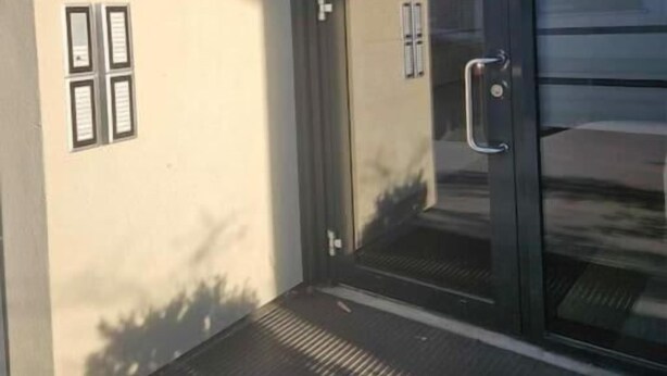 Une entrée moderne avec une porte en verre, une poignée en métal et un petit luminaire extérieur.