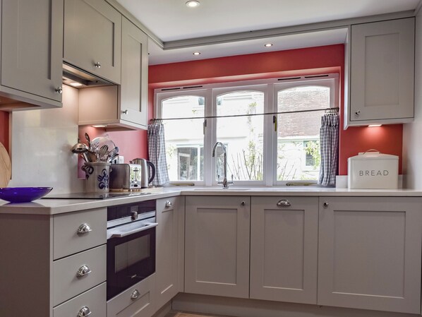 Una cocina moderna con armarios blancos, horno empotrado y ventana con cortinas.