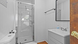 Un baño con mampara de vidrio, inodoro, lavamanos y espejo.