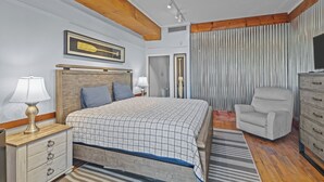 Un dormitorio con cama de cabecera de madera, lámparas de noche, televisor, una silla y un aparador.