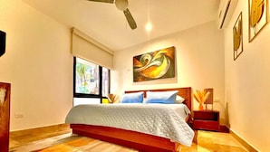 A bedroom with a bed, a window, a ceiling fan, and a painting on the wall.