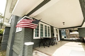 A covered patio with a brick exterior, a table and chairs, and an American flag. - Walk to Restaurants - Trendy Lakeview Craftsman (Birmingham)