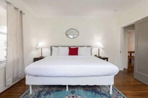 A neatly arranged bedroom with a bed, two bedside lamps, a mirror above the bed, and a patterned rug.