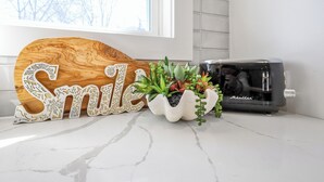 Uma bancada de cozinha com uma placa de madeira com a palavra 'Smile', um vaso de cerâmica branca com suculentas e uma torradeira preta.