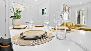 Uma área de refeições moderna com uma mesa de mármore, pratos brancos, copos transparentes e um vaso de flores brancas.