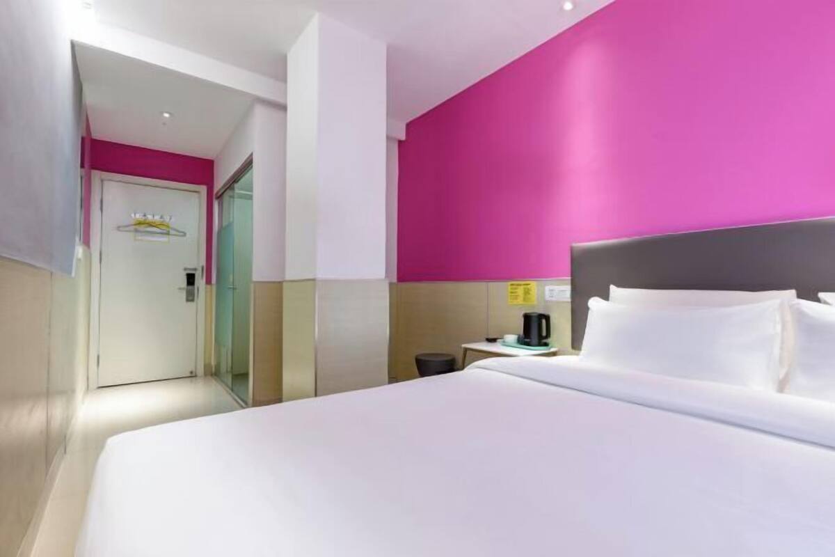 A hotel room with a bed, a nightstand, a coffee maker, and a door.